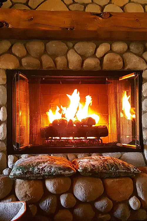 a fire burning in a stone fireplace with pillows.        